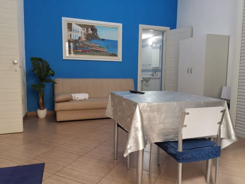 Studio Blu apartment with blue accent wall, beige sofa, dining table, and bathroom at Casa Vacanze Del Golfo in Castellammare