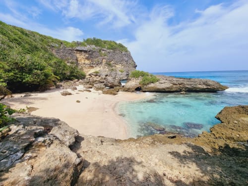 Prístina cala de playa turquesa con arena blanca, acantilados de piedra caliza y vegetación exuberante cerca de Gites Kaladja en Port-Louis,
