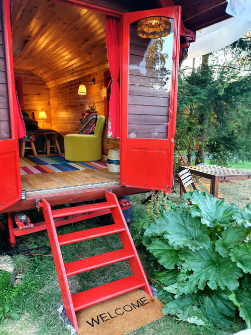 Red vintage caravan with open doors revealing cozy interior, welcome mat, garden setting at Les Refuges Du Chalet in Jalhay