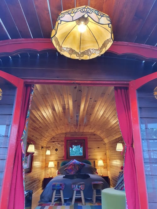 Pink caravan bedroom interior at Les Refuges Du Chalet in Jalhay with wooden walls, decorative lamp, and garden view