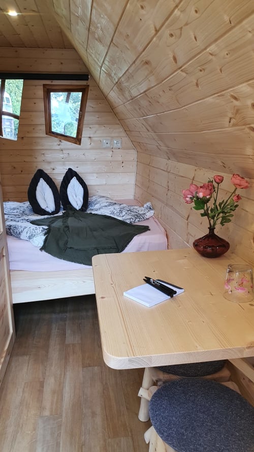 Gemütliches Holzhausinterieur in Les Refuges Du Chalet mit Bett, Schreibtisch, rosa Blüten in der Vase und Gartenblick