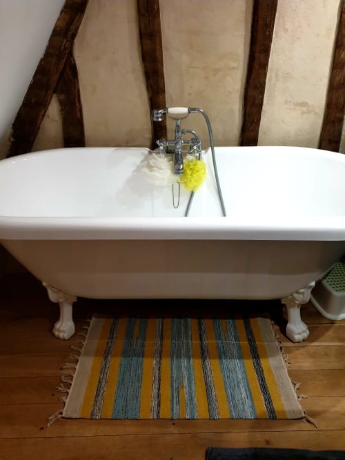 Baignoire ancienne à pieds griffus avec robinetterie chromée à La Dragonne B&B à Bellême, France, avec tapis de salle de bain rayé et