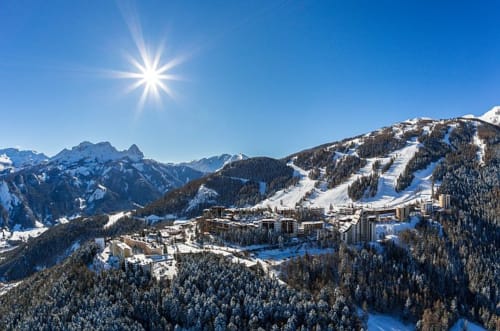 Vue aérienne de l'Hôtel MarjoRI à Le Lauzet-Ubaye enneigé, avec pistes de ski et montagnes alpines sous un beau soleil