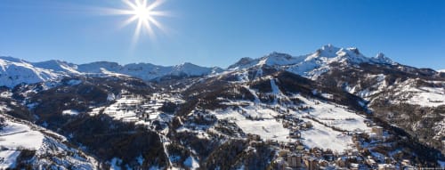 Paysage alpin enneigé du Lauzet-Ubaye avec montagnes, pistes de ski et chalets dispersés sous un soleil éclatant
