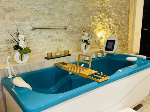 Luxueux bain à remous bleu avec tablette en bois et accessoires blancs dans la salle de bains du cottage Gindou