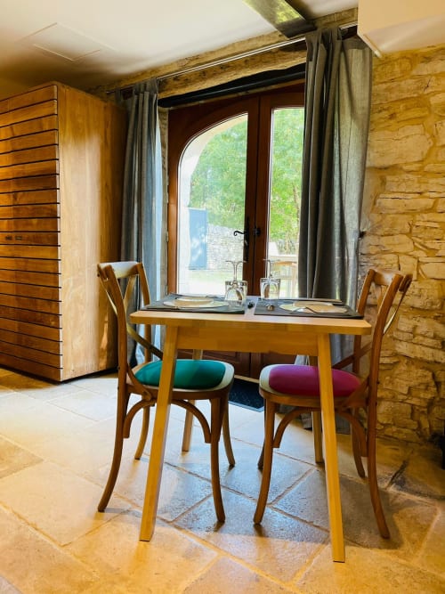 Salle à manger du cottage Gindou avec table en bois, chaises colorées et portes-fenêtres donnant sur le jardin