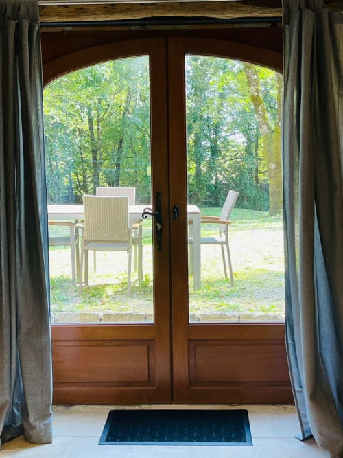 Portes en bois s'ouvrant sur une terrasse avec chaises et arbres au gîte Vue Sur Gindou à Gindou, France