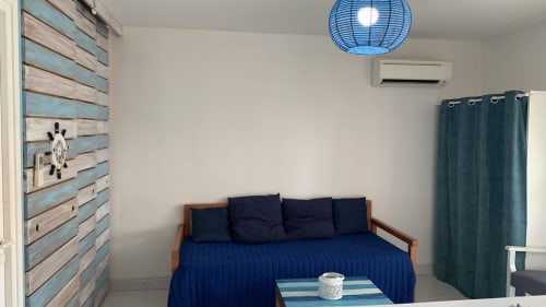 Chambre douillette de l'appartement Caribluewave avec lit bleu, mur d'accent en bois, luminaire suspendu bleu et rideaux turquoise