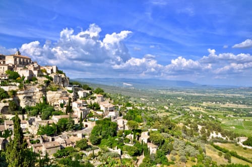 Gordes village perched on hilltop with stone buildings, cypress trees, and Provence valley landscape below