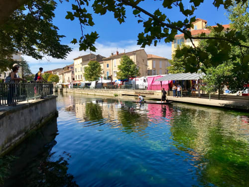 Picturesque canal in Gordes, France with traditional stone buildings and market stalls reflected in clear blue water