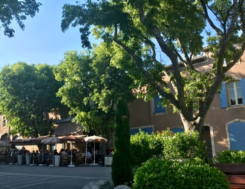 Outdoor café seating under shade trees at Provence Km28 bed and breakfast in Gordes, France with terracotta buildings