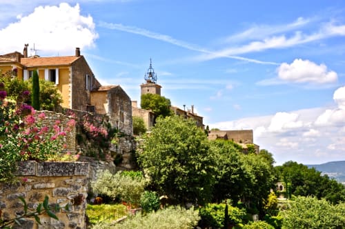 Charming stone village of Gordes in Provence with historic buildings, church tower, blooming flowers, and rolling hills under
