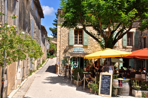 Charming Provençal street in Gordes with stone buildings, outdoor dining under yellow umbrellas at Provence Km28 restaurant