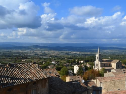 Aerial view of Gordes village with stone buildings, church spire, and Provence countryside under blue sky