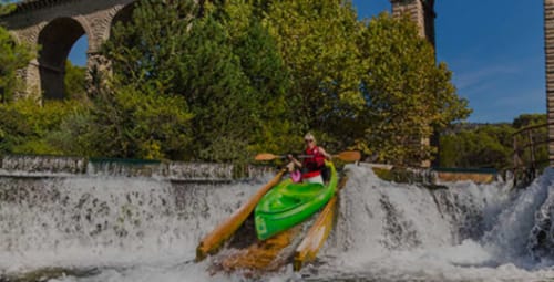 Personne en kayak sur la voie navigable de Gordes près de Provence Km28, avec architecture en pierre historique et végétation luxuriante