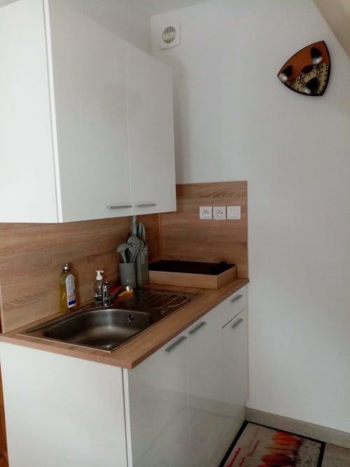 Petite kitchenette avec plan de travail en bois, évier, mobilier blanc et porte-ustensiles dans la Chambre de luxe aux Clématites