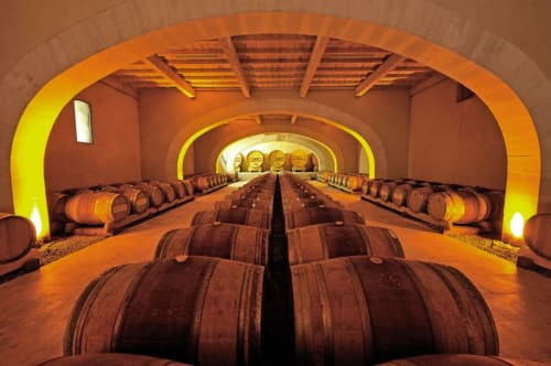 Cave de barriques à la Provence Km28 à Gordes, éclairage orange chaleureux et rangées symétriques de fûts de chêne