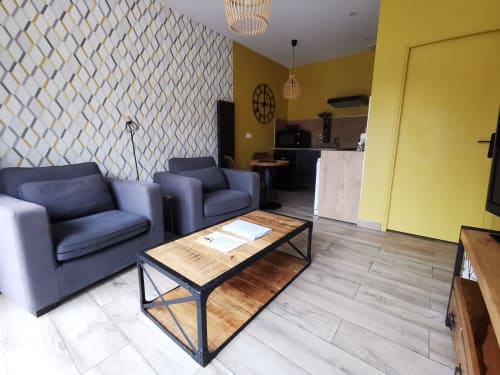 Salon contemporain du gîte La Cour d'Hortense avec sièges bleus, table en bois, cuisine jaune et papier peint à motifs