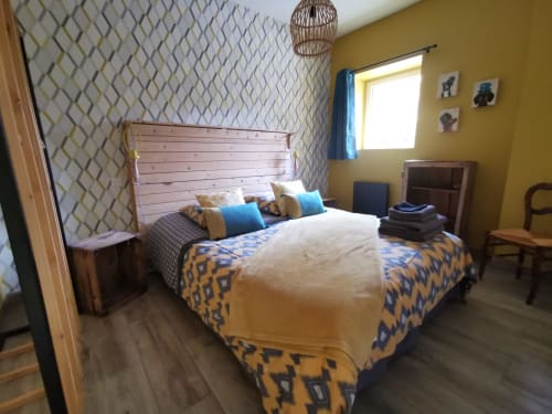 Chambre lumineuse du gîte La Cour d'Hortense en France avec murs jaunes, literie à motifs géométriques et lit en bois