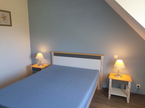 Chambre douillette à Loc'Maria, Belle Île en Mer, avec lit bleu, tête de lit blanche, lampes de chevet et vue sur mer