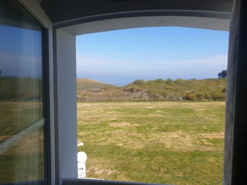Vue sur la mer depuis le balcon de l'appartement à Locmaria, Belle Île-en-Mer, avec prairie verdoyante et collines côtières