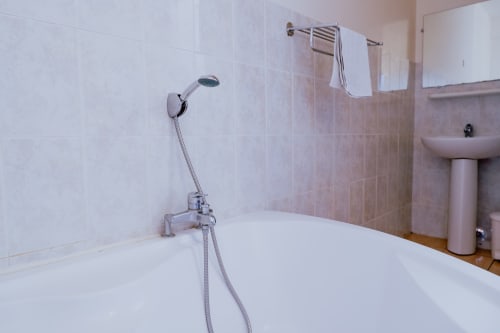 Salle de bain moderne avec baignoire blanche, douchette et porte-serviettes à l'Hôtel du Cirque à Cilaos