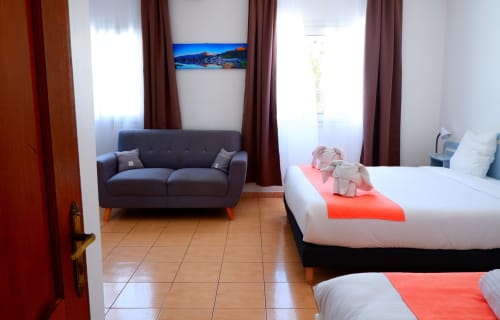 Chambre triple à l'Hôtel du Cirque à Cilaos avec lits jumeaux, canapé et vue sur les montagnes