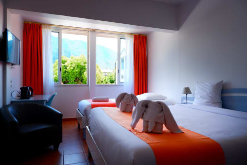 Chambre triple lumineuse à l'Hôtel du Cirque à Cilaos avec deux lits, vue sur les montagnes, touches rouges et équipements modernes