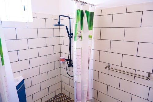 Douche carrelée de blanc avec joints noirs à l'Hôtel du Cirque, Cilaos, dotée d'une pomme de douche pluie bleue et verte