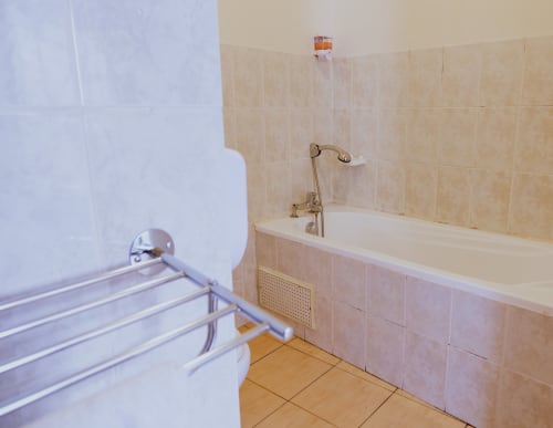Salle de bain de l'Hôtel du Cirque à Cilaos avec baignoire, rideau de douche blanc, carrelage beige et plancher en bois.