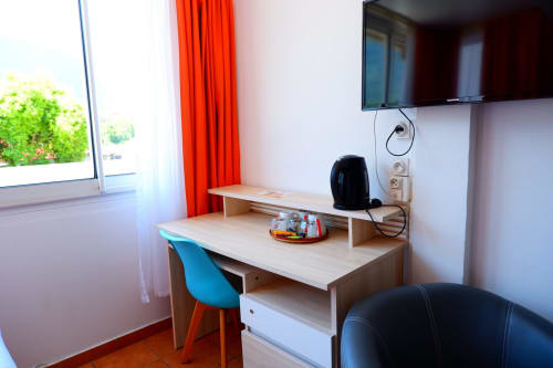 Chambre triple de l'Hôtel du Cirque avec espace de travail, bureau, chaise bleue, TV et vue sur les montagnes depuis la fenêtre à Cilaos