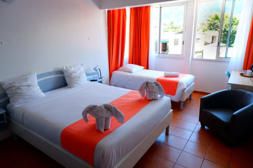 Chambre triple lumineuse à l'Hôtel du Cirque de Cilaos avec lits jumeaux, touches rouges, vue montagne et équipements modernes