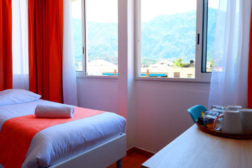Chambre lumineuse à l'Hôtel du Cirque à Cilaos avec lit simple, accents rouges et vue panoramique sur les montagnes