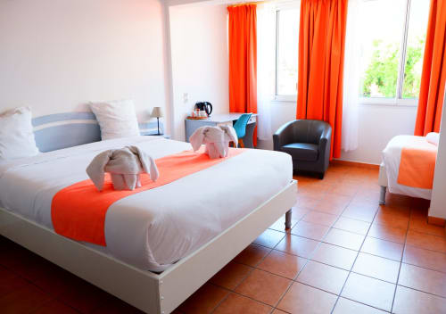 Chambre triple lumineuse à l'Hôtel du Cirque avec lits jumeaux, accents orangés, coin salon et vue sur les montagnes