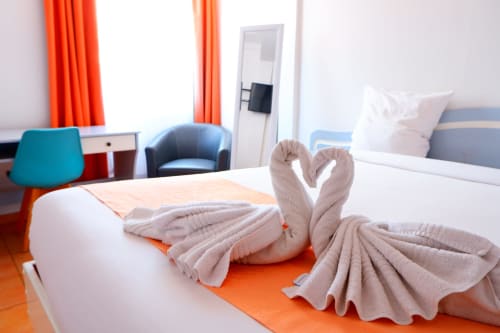 Chambre moderne de l'Hôtel du Cirque avec cygnes en serviettes, touches orange et vue sur les montagnes à Cilaos