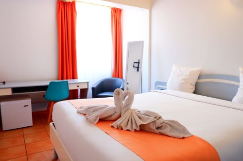Chambre moderne de l'Hôtel du Cirque à Cilaos avec lits jumeaux, accents orange, bureau et vue sur les montagnes à travers des rideaux rouges