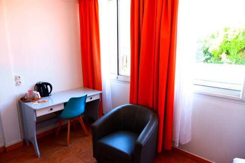 Chambre double de l'Hôtel du Cirque à Cilaos avec bureau, chaise turquoise, fauteuil noir et rideaux rouges vue montagne