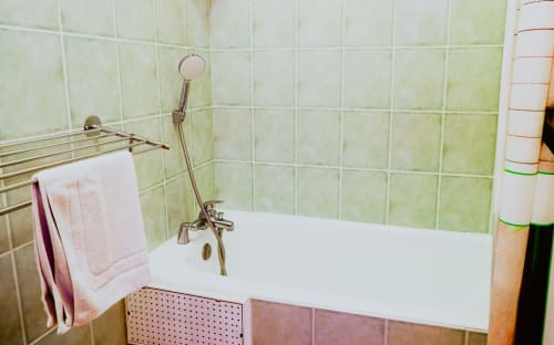 Salle de bains de l'Hôtel du Cirque avec baignoire blanche, carrelage vert, pommeau de douche amovible et porte-serviettes