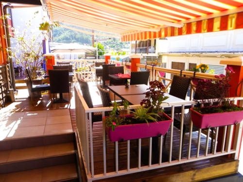 Terrasse animée de l'Hôtel du Cirque avec auvent rayé, tables de restaurant, jardinières roses et vues sur les montagnes à Cilaos