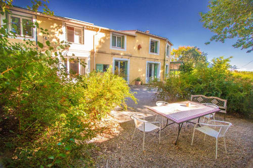 Cour du gîte Sylvie Cambon à Montséret avec table de repas, chaises et maison en pierre jaune entourée de verdure