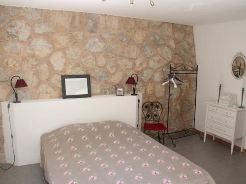 Chambre accueillante du gîte Sylvie CAMBON à Montséret avec parure florale, tête de lit blanche et mur en pierre rustique