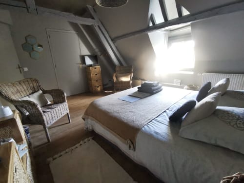 Chambre lumineuse sous les toits à La Cour d'Hortense avec lits, fauteuil en rotin et vue sur le jardin.