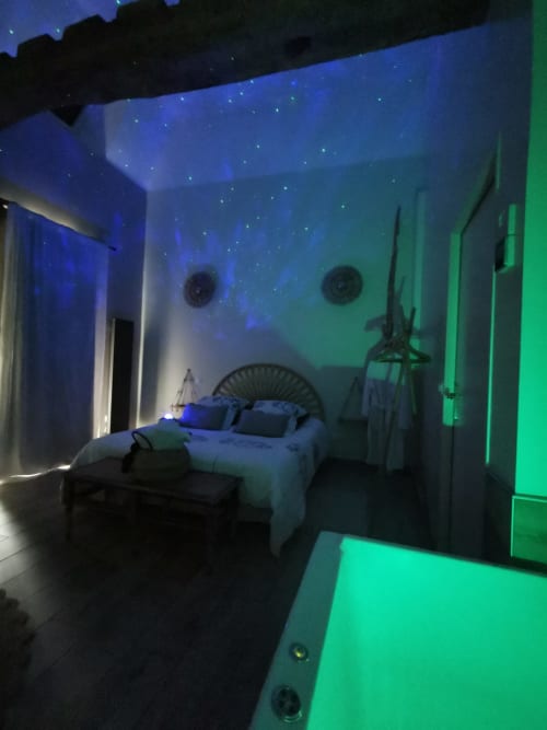 Chambre contemporaine à La Cour d'Hortense avec éclairage ambiant bleu et vert, lit garni de coussins et projection de ciel étoilé au plafond