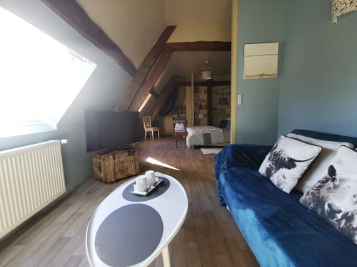 Chambre mansardée à La Cour d'Hortense avec lit bleu, télévision et coin salon
