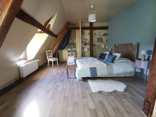 Chambre spacieuse sous les toits à La Cour d'Hortense avec poutres apparentes, lit queen-size, rangements et vue sur le jardin.