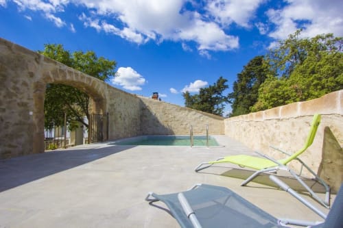 Espace piscine de Sylvie CAMBON à Montséret avec transats, murs en pierre et ciel bleu dégagé