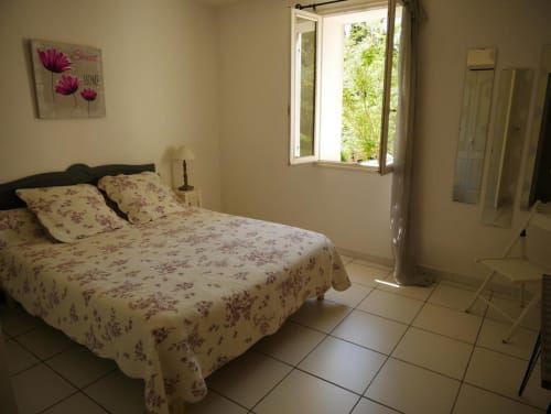 Chambre lumineuse à la maison d'hôtes Sylvie Cambon à Montséret, avec literie fleurie, fenêtre ouverte sur la verdure et décoration accueillante.