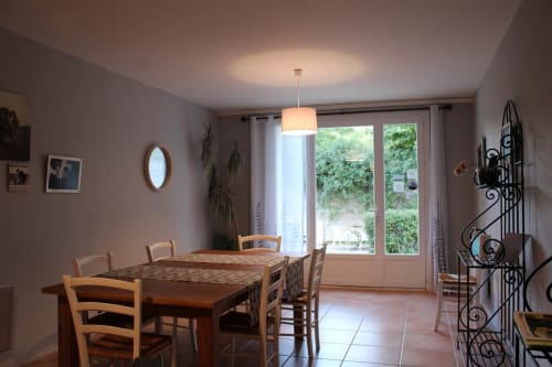 Salle à manger lumineuse à la maison d'hôtes Sylvie CAMBON à Montséret avec table en bois, chaises, suspension et portes vitrées donnant sur