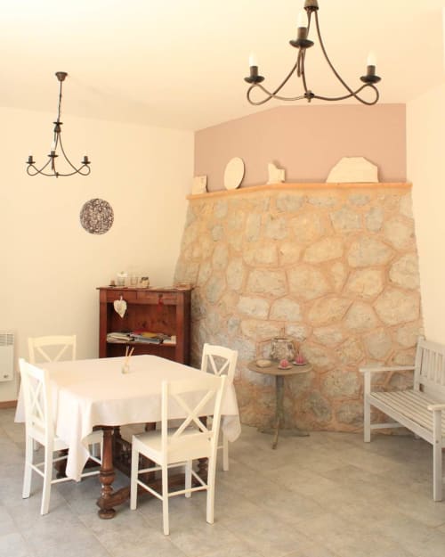 Élégante salle à manger de la chambre d'hôtes Sylvie CAMBON à Montséret avec cheminée en pierre, chaises blanches et lustres vintage