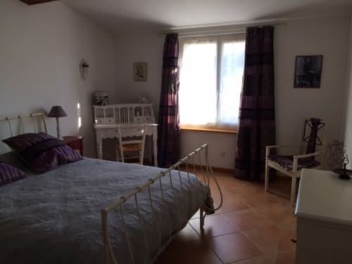 Spacieuse chambre de la maison d'hôtes Sylvie CAMBON à Montséret avec lit en fer, bureau, rideaux violets et sol en terre cuite